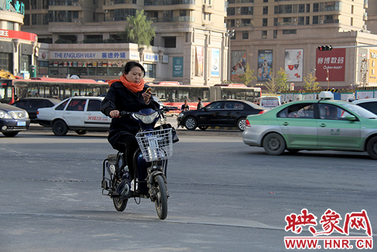 一名女士騎著電瓶車看著手機