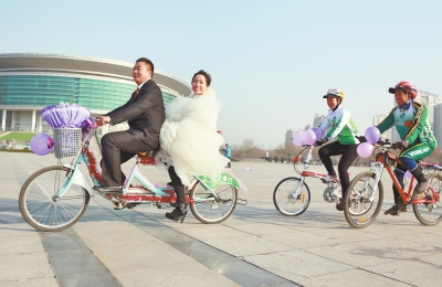 氣球和鮮花裝點(diǎn)的雙人自行車，新郎郝幸福載著美麗新娘回家。