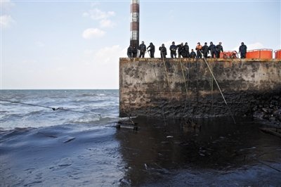 昨日，山東青島，清污人員正在海邊清理油污。