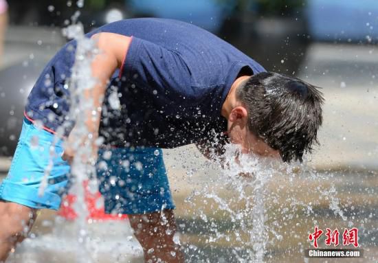 5月29日，一名小孩將頭伸向北京街頭的噴泉以降溫祛暑。