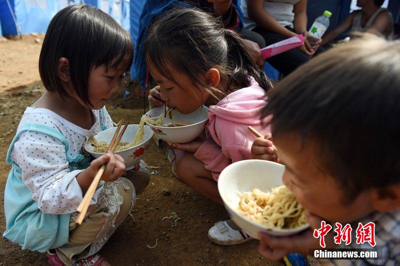 2014年8月6日，云南魯?shù)辇堫^山災(zāi)區(qū)，兒童在帳篷外吃飯。