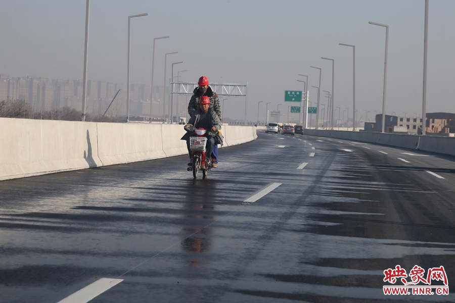 兩名工人騎車經(jīng)過灑水養(yǎng)護(hù)路面。