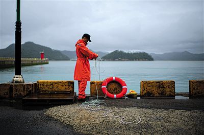 7月6日，韓國(guó)珍島，一名海岸警察在港口系救生圈。4月，客輪在珍島近海發(fā)生沉船事故后，仍有11人下落不明。